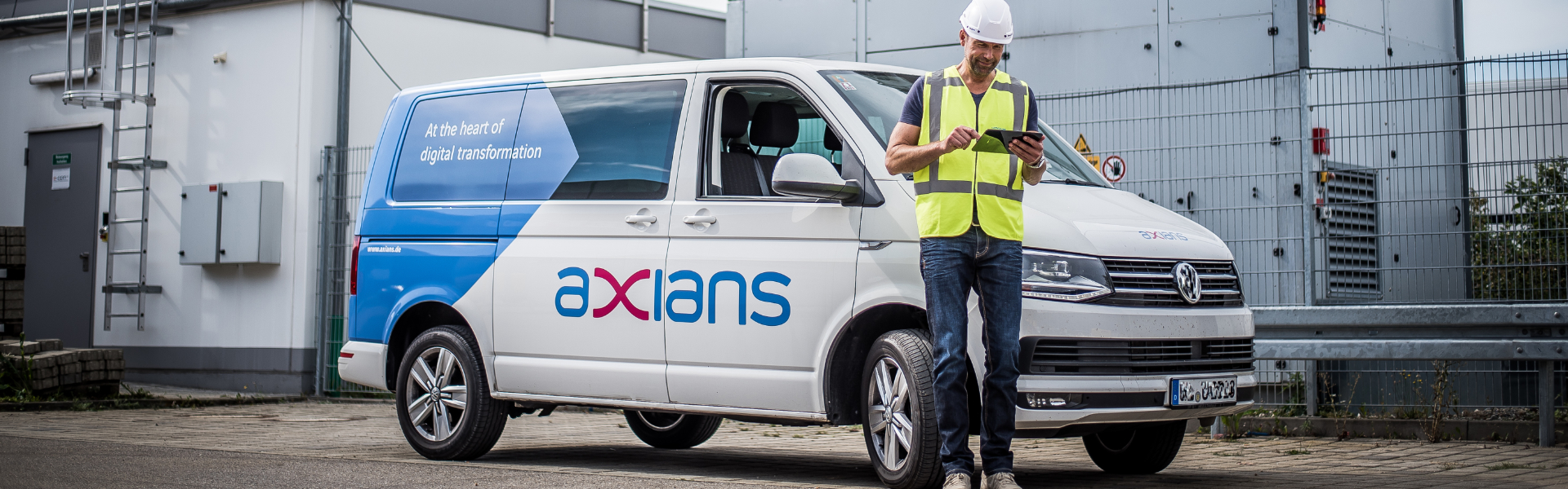 Techniker mit Tablet steht vor Axians Kastenwagen